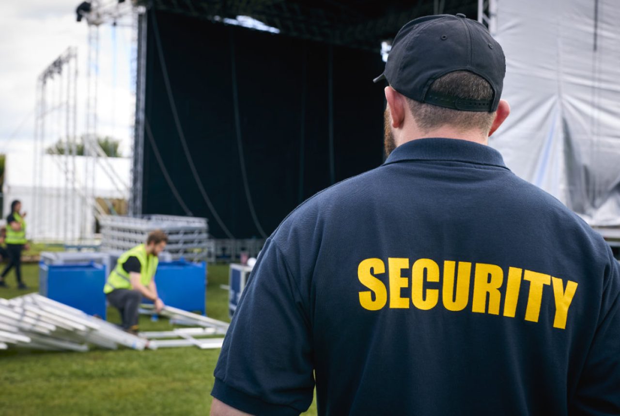 Rear View Of Security Team At Outdoor Stage For Music Festival Or Concert